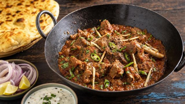 Lamb karahi, Lahori Butt style, in a black iron karahi with naan, onions and raita