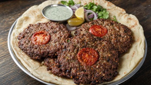 Peshawari chapli kebab with tomato slices on naan with onions, lemon and mint chutney